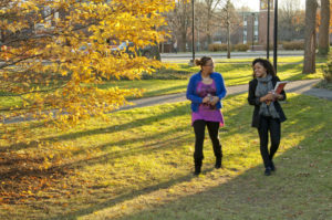Two students Yahaira Murphy and walking next to Carroll Hall at sunset with Clocktower in background.