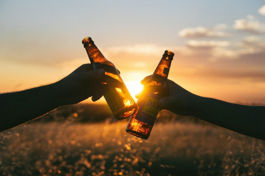 Two people clinking beer bottles together in front of a sunset