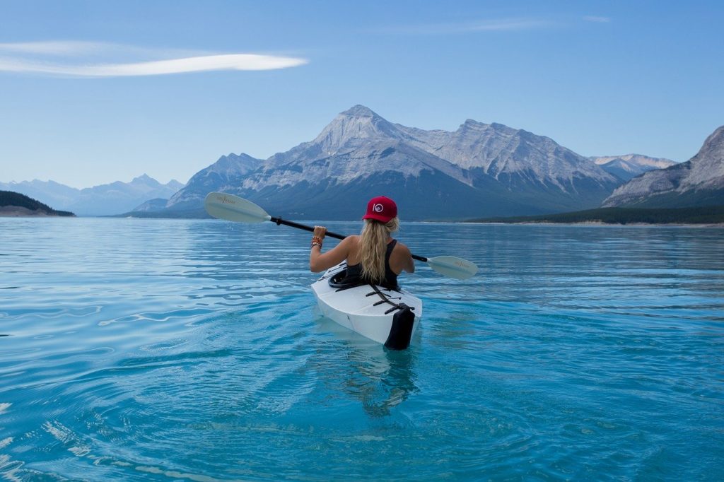 Person in a white kayak kayaking in front of mountains