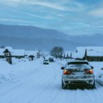 Car driving down a snow-packed road towards a set of mountains.