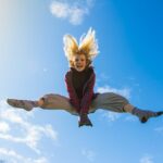 Woman jumping in the air with her legs out on a blue sky background.