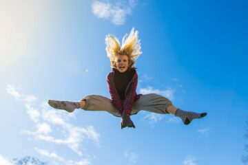 Woman jumping in the air with her legs out on a blue sky background.