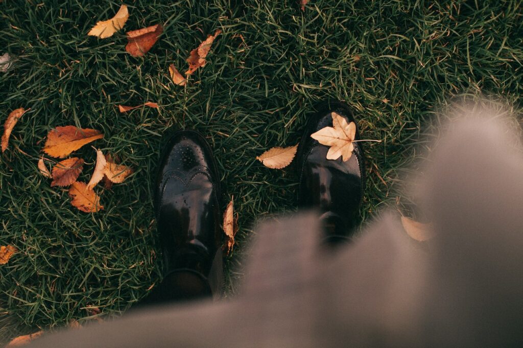 A point of view shot looking down at black shoes amidst fall leaves.
