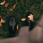 A point of view shot looking down at black shoes amidst fall leaves.