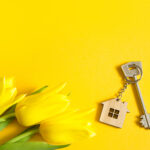 Key ring in the shape of wooden house with key on yellow background and spring tulips.