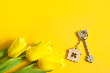 Key ring in the shape of wooden house with key on yellow background and spring tulips.