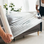 cropped view of movers holding stretch film roll near sofa