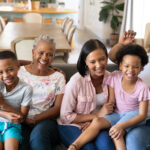 A multigenerational family sitting on a couch, smiling and enjoy each other's company.