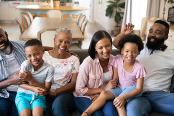 A multigenerational family sitting on a couch, smiling and enjoy each other's company.